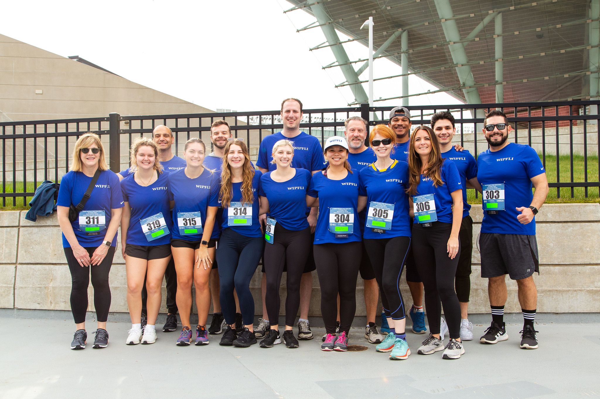 Members of the Wipfli team assemble for an outdoor racing event. They wear matching blue shirts and participation numbers.