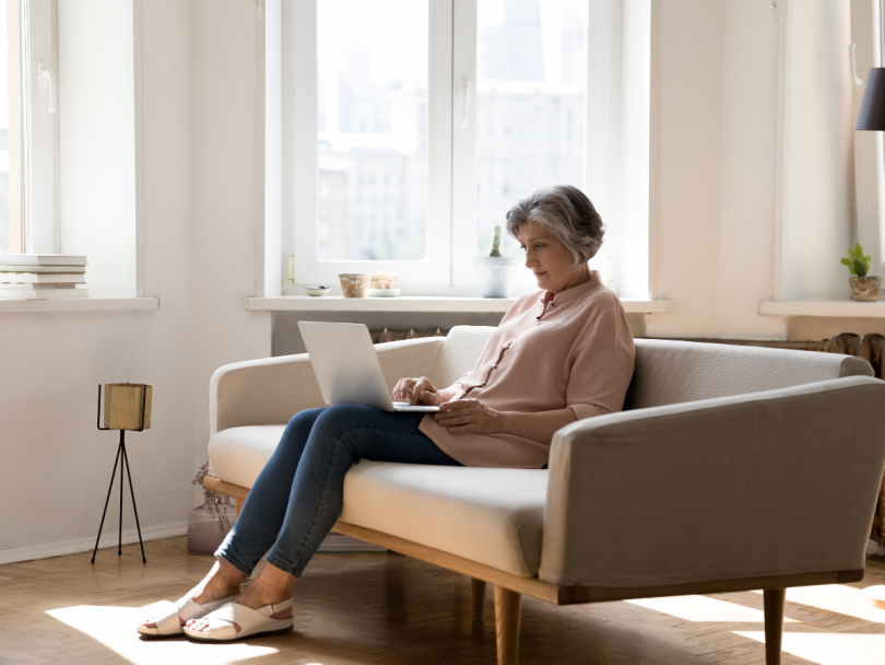 A woman sitting on her couch making a doctor’s appointment on her laptop