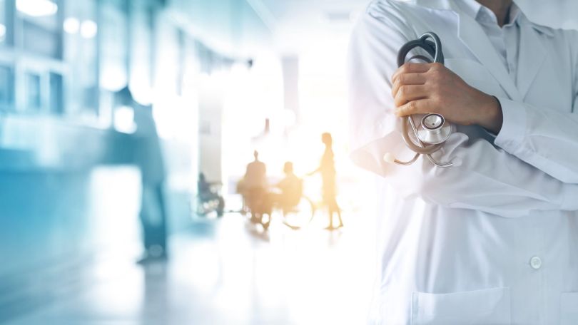A medical professional stands with patients in the background.